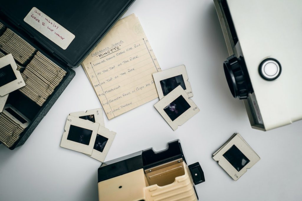A box of old photos and a camera on a table, offering personal touch printing.