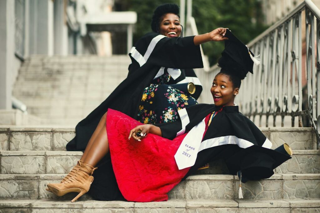 Two women in graduation gowns sitting on steps, capturing the moment with Party Photos With Printing On Site.