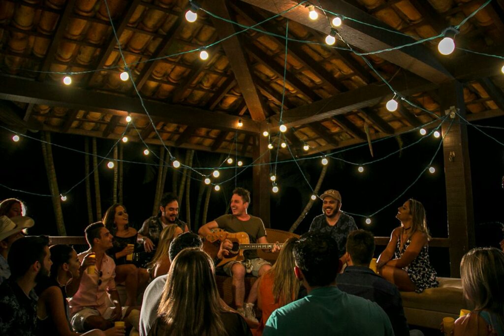 A group of people enjoying the ambiance of string lights on a wooden deck while memorial programs and posters are being discussed.