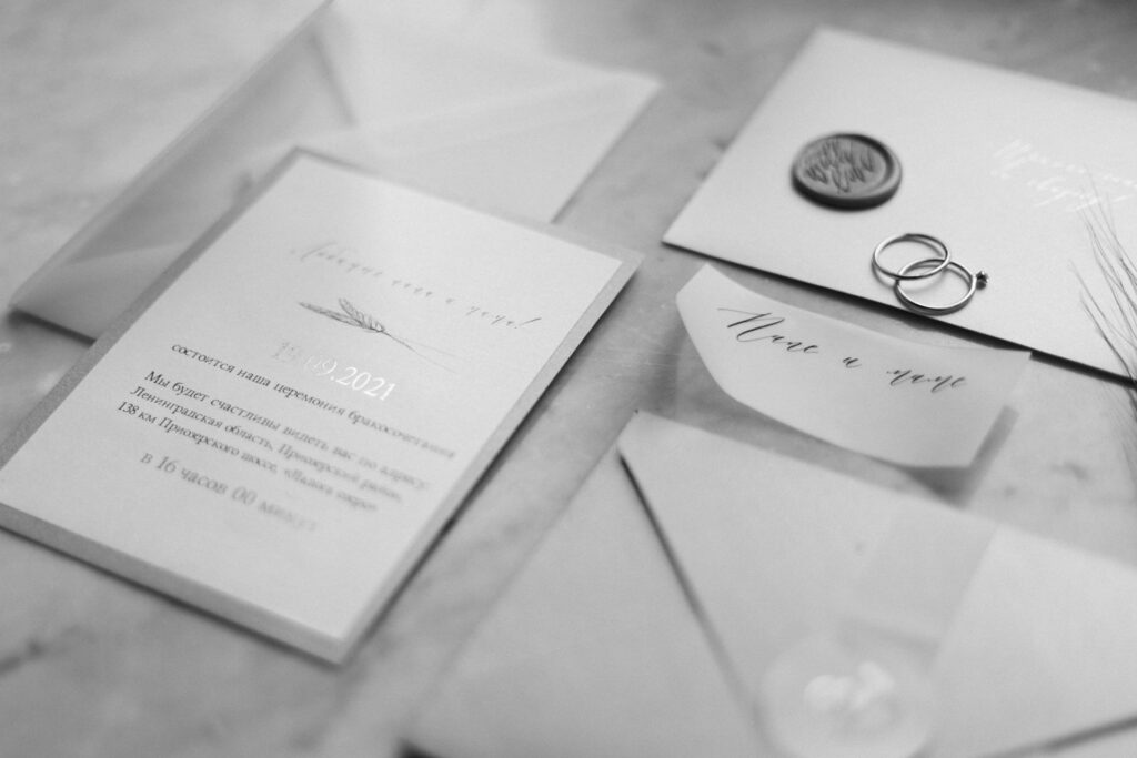 Black and white photograph of a wedding invitation with date and details, accompanied by envelopes, a wax seal, and wedding rings, featuring Personal Touch Printing.